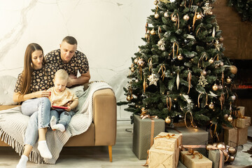 a family sits on the sofa near a beautifully decorated New Year tree. dad, mom and little son in the living room decorated for Christmas. Christmas.  New Year