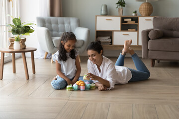 Indian mother and little daughter play together use toy set dishware and plastic sweets, spend...