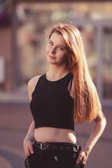 Summer portrait of a young beautiful long-haired girl in dark clothes in an urban environment.
