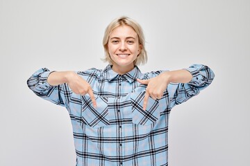 Young blond woman in casual pointing down finger, demonstrating empty space for product or text...