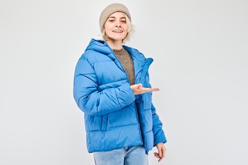 Young woman in blue winter jacket holding something in hand, demonstrating empty space for product...