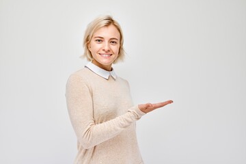 Young blond woman in casual holding something in hand, demonstrating empty space for product or...
