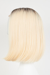 Naklejka premium Natural looking blonde fair wig on white mannequin head. Middle length hair cut on the plastic wig holder isolated on white background, side view.