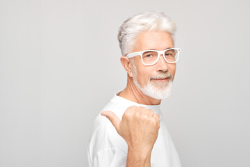Gray-haired mature man 60 years old in white T-shirt pointing aside finger, demonstrating empty...