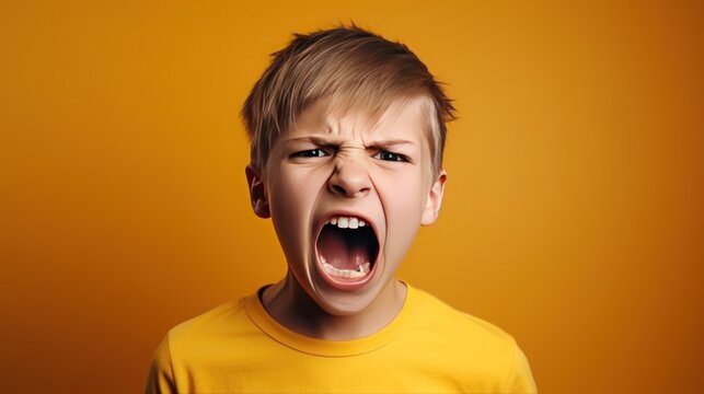 Angry irritated boy on yellow background. Full of rage. Emotional portrait of an upset preteen boy screaming in anger. Requirements for parents. Wrong perception. Hysterics.
