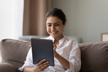 Cute Indian woman holding digital tablet, make on-line purchase, enjoy distancing communication via social media network, share messages, do e-shopping buying goods and items for home. Tech concept