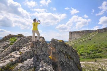 A woman stands on a large rock and takes a photo of the White Rock. Crimea
