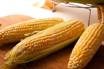 Clous up view of cutting board with three cobs sweet corn on white wooden background..