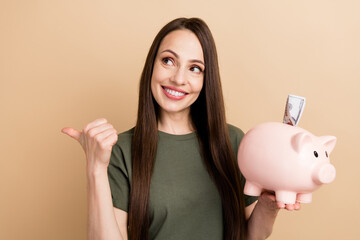 Photo of young woman t shirt direct finger empty space hold piggy wallet more earnings percent in bank isolated on beige color background