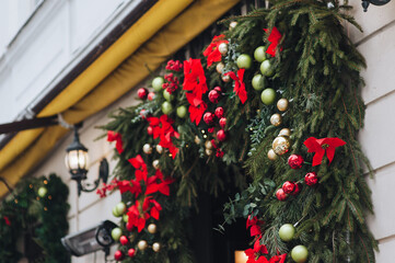 The natural, bright green Christmas tree is adorned with large red flowers and small decorative balls above the doorway. The concept of New Year holidays. Handmade background.