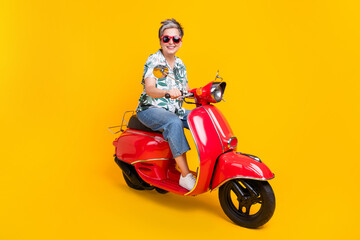 Full size photo of attractive senior woman riding red motorcycle wear trendy tropical print clothes isolated on yellow color background