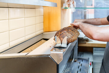 Professional baker slices a crusty artisan loaf with an industrial bread slicer in a clean bakery...