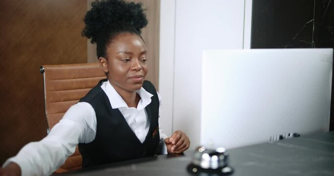Portrait of cute African female receptionist in luxury hotel using computer to administrate and taking calls from customers. Professional elegant woman in suit working as administrator.