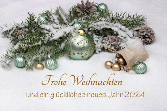 Weihnachtskarte: Grüne Weihnachtskugeln mit Tannenzweigen und Weihnachtsdekoration auf einer Schneedecke mit dem Text Frohe Weihnachten und ein glückliches neues Jahr 2024.