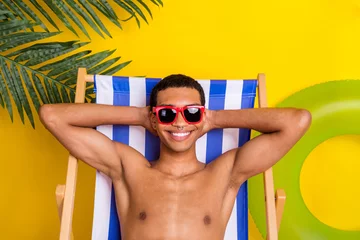 Fotobehang Photo of positive charming shirtless man dark glasses having rest lounge chair arms behind head isolated yellow color background © deagreez