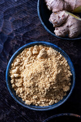 Ginger powder placed in a ceramic bowl and ginger roots