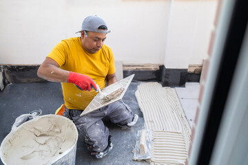 builder on his knees putting cement on the tile preparing for installation