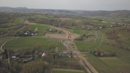 Fototapeta premium Laying gas pipeline among green hills. Large high-pressure steel pipes prepared for immersion in the excavated trench. Land works in the strategic industry. Energy and natural resources