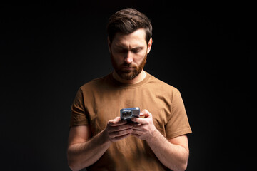 Serious bearded man holding mobile phone text message, communication online isolated on black background. Technology concept 