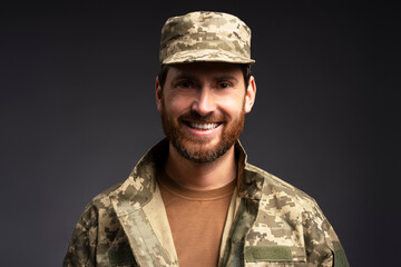 Closeup portrait smiling confident  bearded soldier wearing camouflage military uniform looking at camera  isolated on black background 