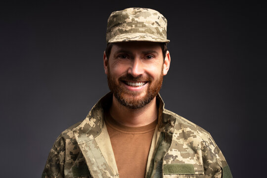 Closeup portrait smiling confident  bearded soldier wearing camouflage military uniform looking at camera  isolated on black background 