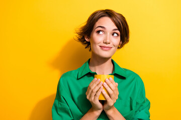 Photo of thoughtful shiny girl dressed green shirt drinking beverage looking empty space isolated yellow color background