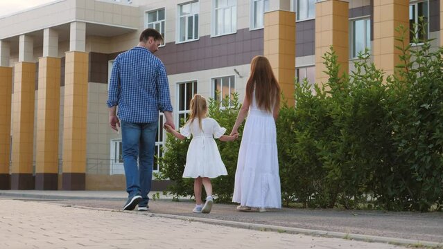 Mother and father take little daughter to school holding hands in city street