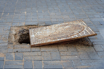 Damaged and open sewer hatch. Accident with sewer hatch in city. Hole on footpath. Broken manhole,...