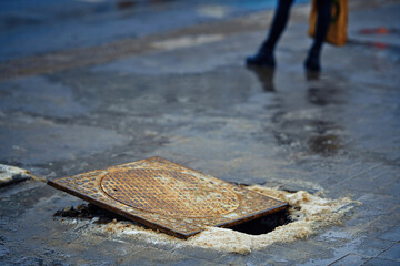 Obraz premium Hole on footpath. Broken manhole, pothole in paving slabs, damaged sidewalk, shifted manhole frame. Damaged and open sewer hatch. Accident with sewer hatch in city. Pedestrian legs on background