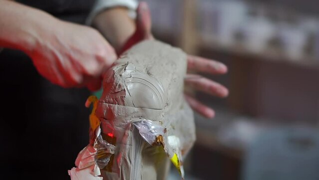 Female hands with a neat red manicure cuts a piece of a block of gray ceramic clay for pottery and tears off it in her workshop. The concept of pottery as a hobby and art