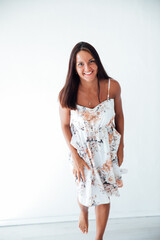 Brunette woman in floral dress posing on white background in room