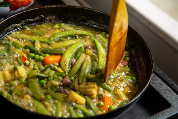 Couscous with vegetables and green beans in a frying pan with a wooden spatula