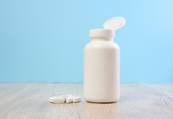 Plastic bottle and oval white pills on the table, blue background
