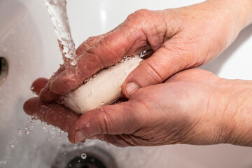 An elderly man washes his hands with soap, wrinkles, old.