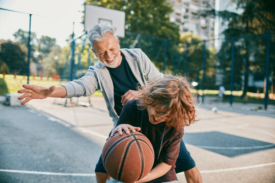 Senior man playing basketball with a young boy at a outdoor basketball court