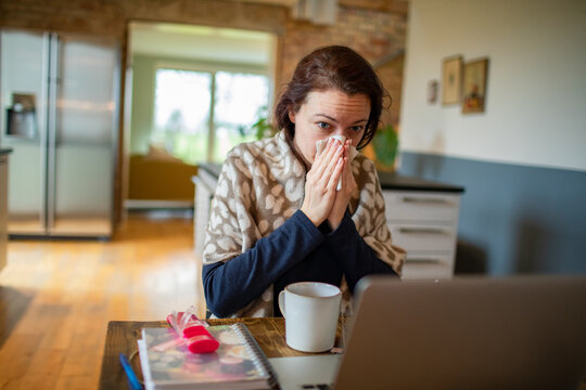Young Woman infected with a cold blowing her nose in a handkerchief at home