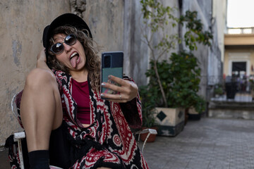 Young Latin American woman with curly hair, hat, sunglasses, funny attitude takes a self-portrait