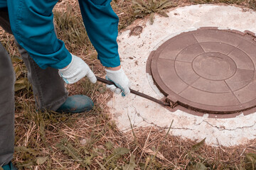 A worker opens a well hatch with a pry bar. Troubleshooting, checking septic tanks