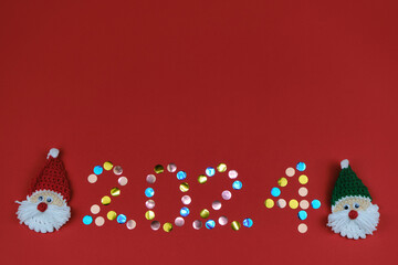 Happy new year 2024 red background with copy space. Round multicolored sequins. Minimalistic Christmas greeting card. Toy amigurumi Santa Claus head.