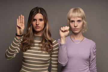 Two women raising hands in a silent plea, showcasing the SOS sign against domestic violence,...
