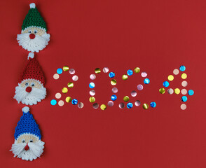 Happy new year 2024 red background with copy space. Round multicolored sequins. Minimalistic Christmas greeting card. Toy amigurumi Santa Claus head.