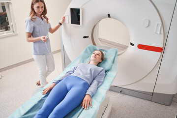 Smiling female doctor talking to woman patient lying on CT scan machine at hospital
