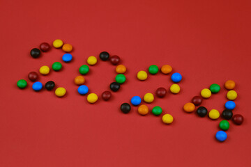 Obraz premium Happy New Year red background, inscription 2024 laid out of round chocolate colored candies. Minimalistic Christmas greeting card.