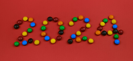 Happy New Year red background, inscription 2024 laid out of round chocolate colored candies. Minimalistic Christmas greeting card.