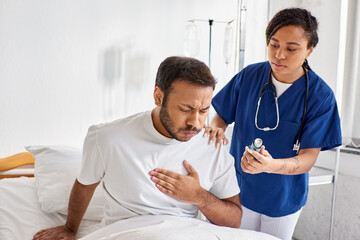 young african american nurse giving asthma inhaler to her ill indian patient in his ward, healthcare - Powered by Adobe
