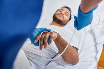 focus on african american nurse setting catheter next to blurred man lying in hospital bed