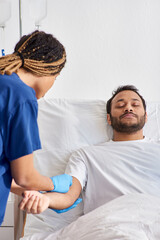 young african american nurse inserting catheter into arm of her sick indian patient, healthcare