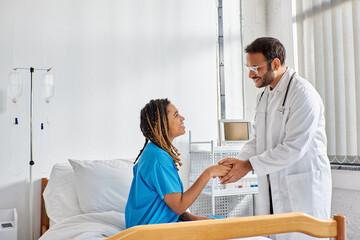 jolly indian doctor in glasses shaking hands with his cheerful african american patient, healthcare