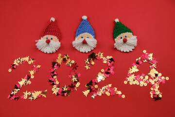 Golden shiny figures of stars and Christmas trees. Knitted toy amigurumi Santa Claus head. Happy new year 2024 red background. Minimalistic Christmas greeting card.
