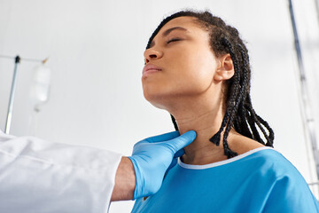 sick pretty african american woman closing eyes while her indian doctor examining her lymph nodes